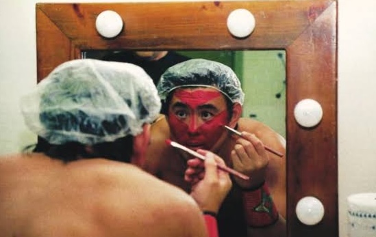 The Great Muta applies his makeup in the mirror. He's wearing a cute little hairnet. 