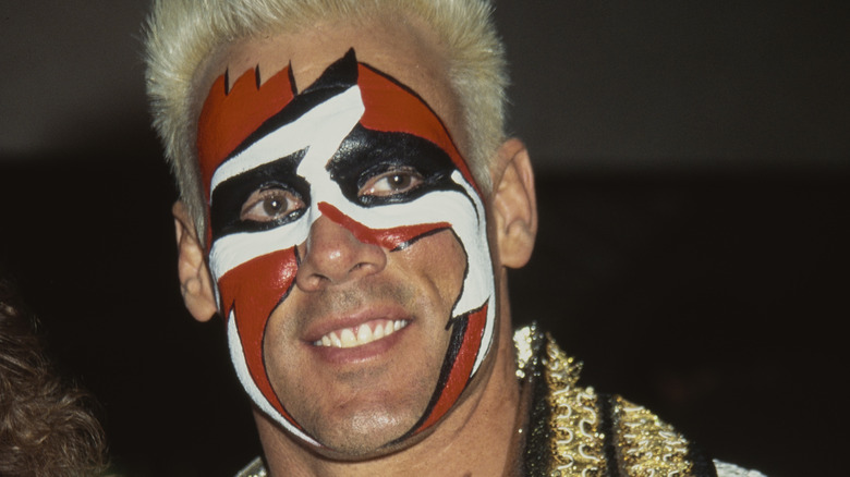 "Surfer" Sting smiles, his face emblazoned in a loud red, white, and black motif. 