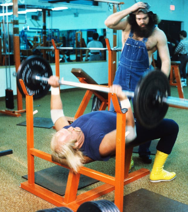 Hillbilly Jim looks on in amazement as Hulk Hogan does bench presses.