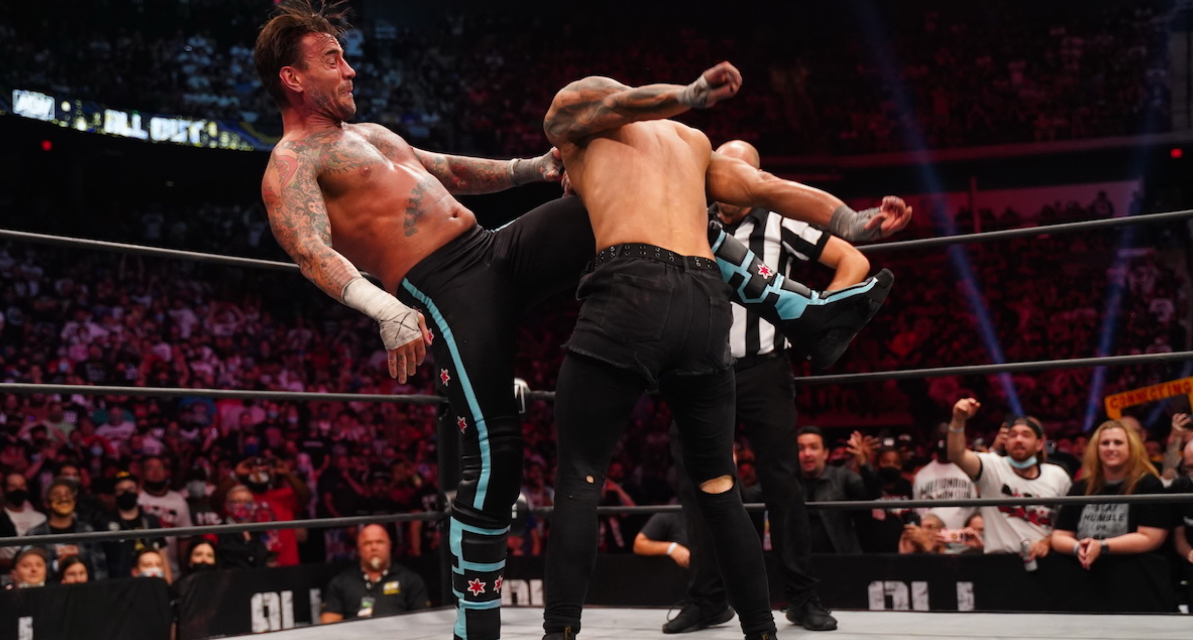 CM Punk lands a GTS on Darby Allin. He is wearing some long wrestling trunks.