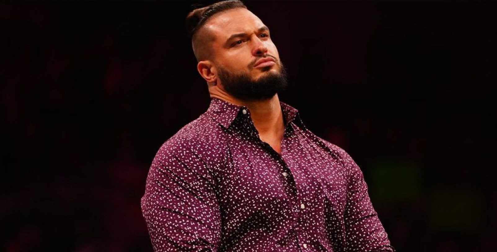 AEW's Wardlow in a fun purple shirt, hair up in a lil topknot.